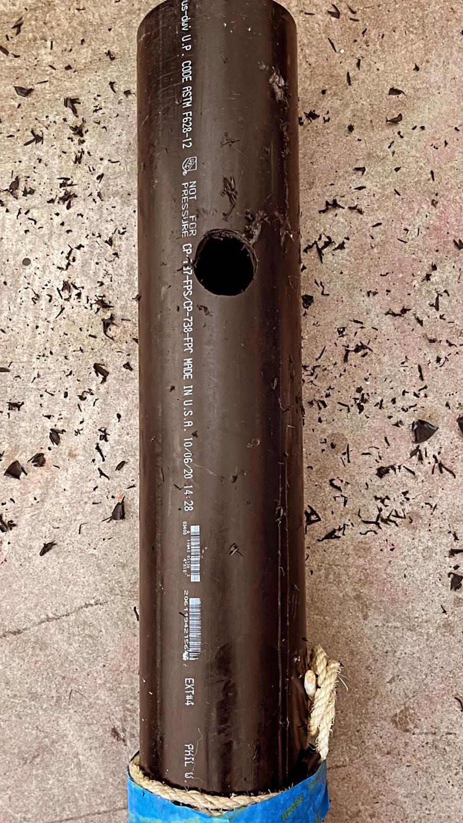 A bare black PVC pipe with a single hole drilled through it.